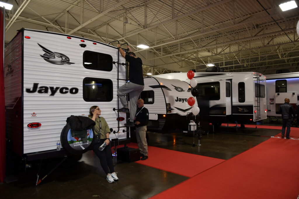 RV Show visitor climbs ladder to inspect trailer roof.